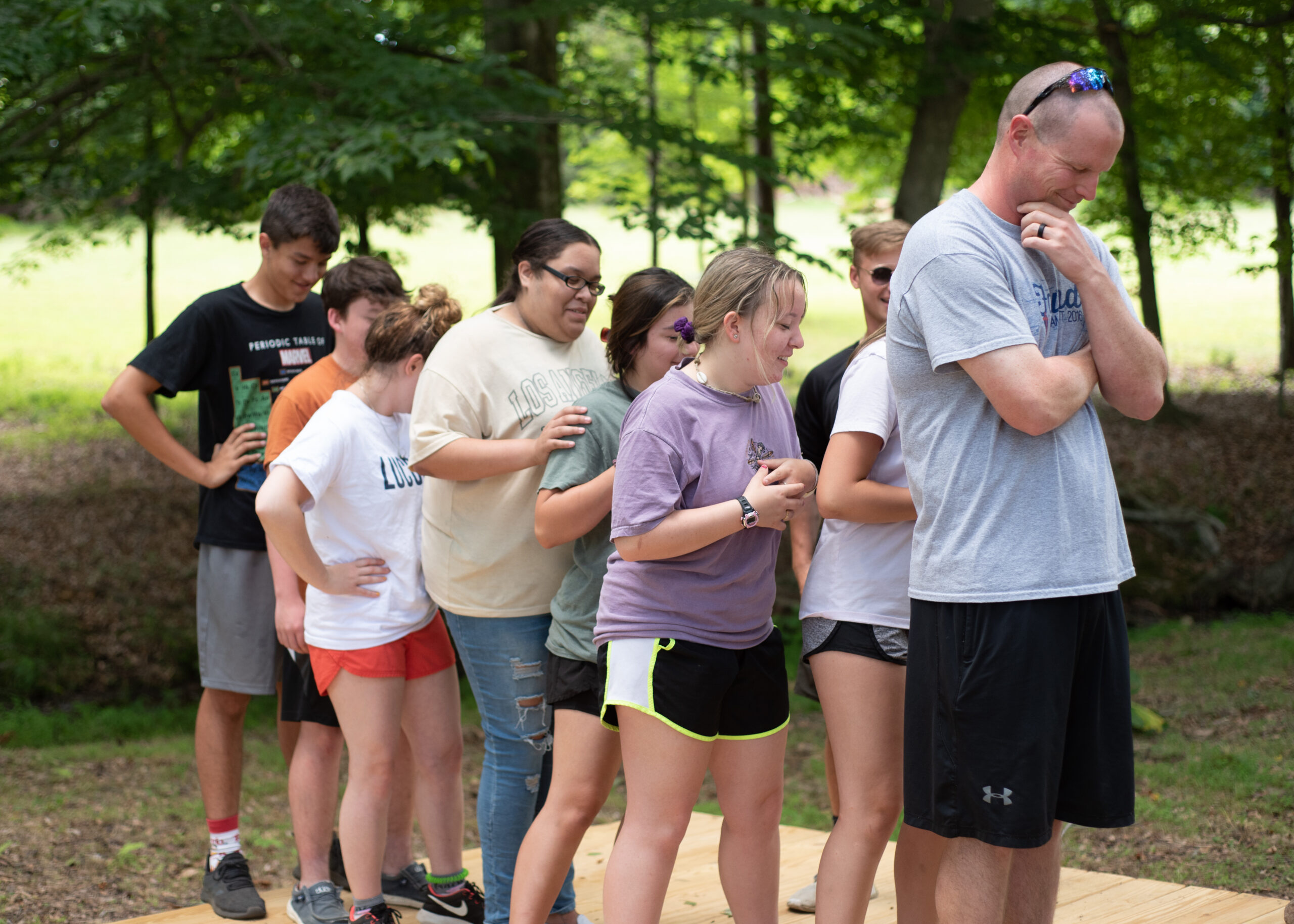 A group of campers and a counselor standing in a line outdoors, engaged in a team-building activity.