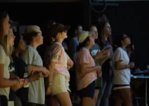 A group of young people gathered for worship in a a dimly lit space.