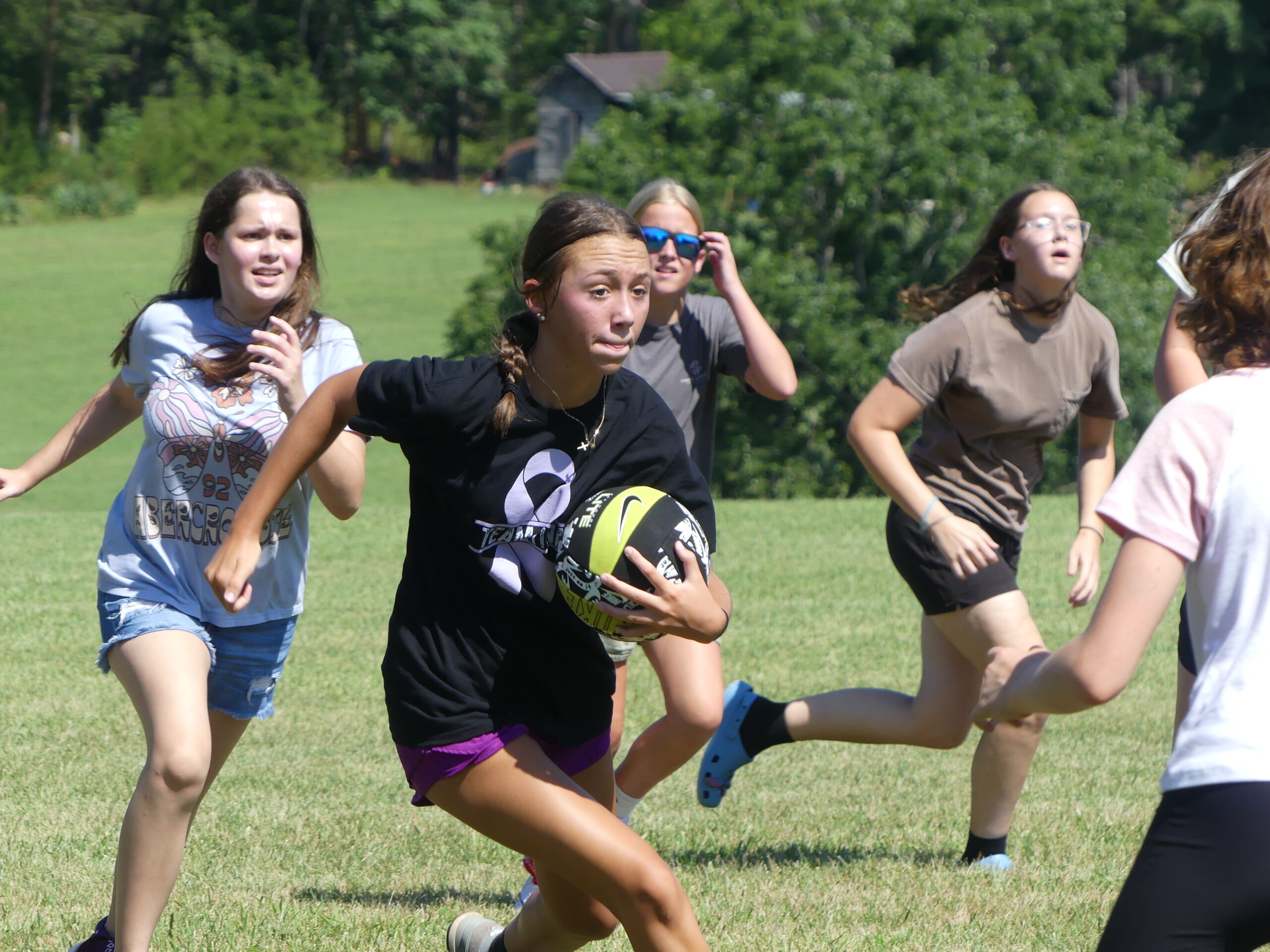 A group of girls play a game of bucket ball outside on a grassy field.