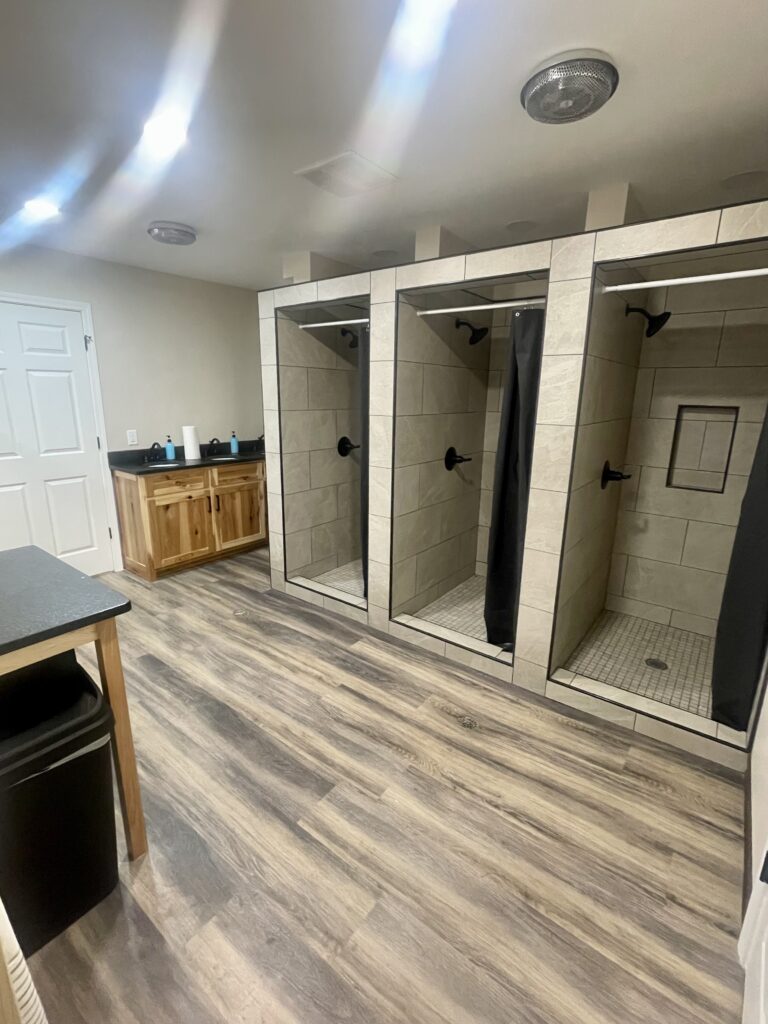 May show: A clean locker room with three tiled shower stalls, a double sink vanity, wood cabinets, and laminate wood flooring.